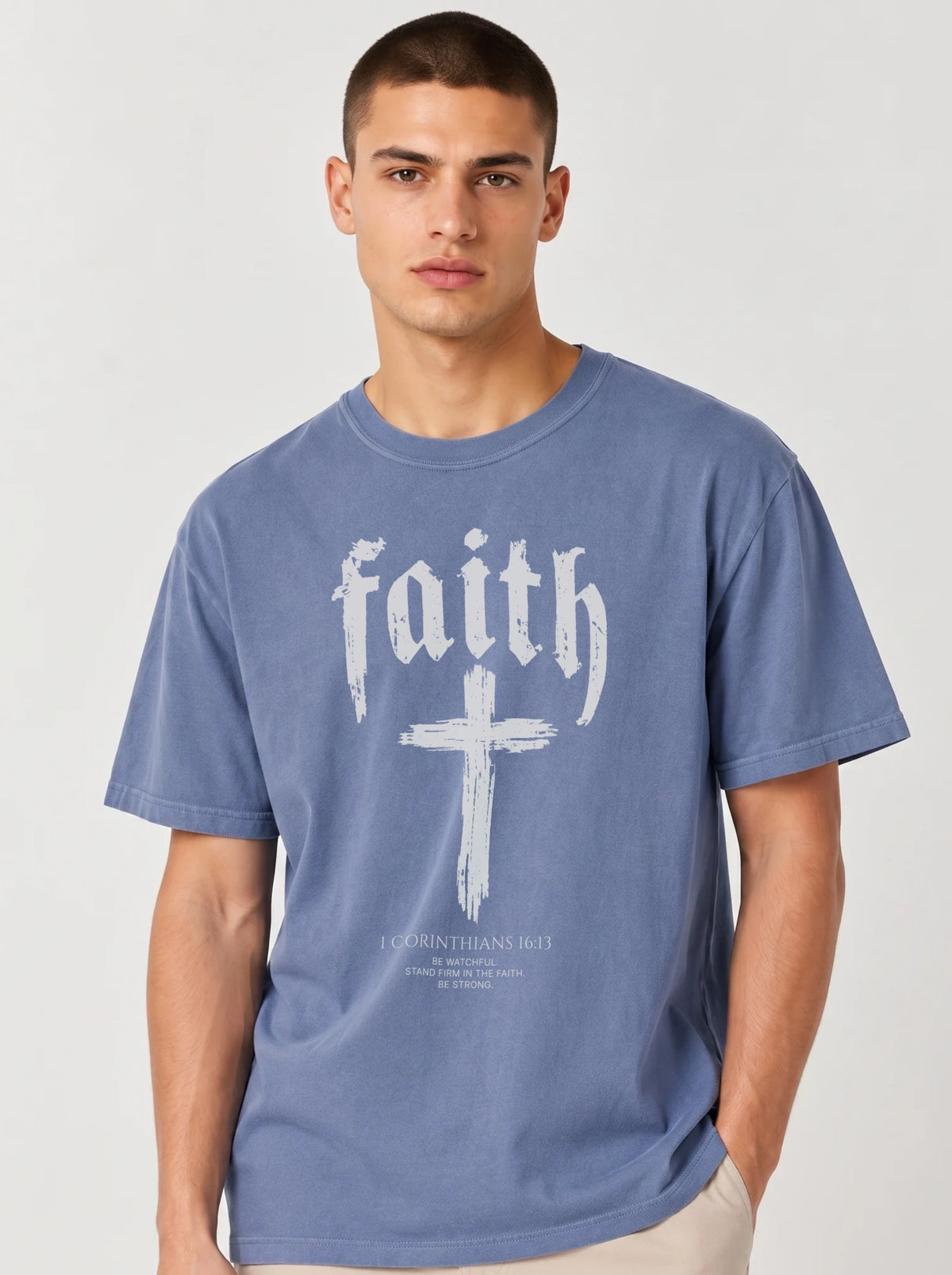 Person wearing a faded blue T-shirt with “faith,” a large cross, and the text “1 Corinthians 16:13 — Be watchful. Stand firm in the faith. Be strong.”