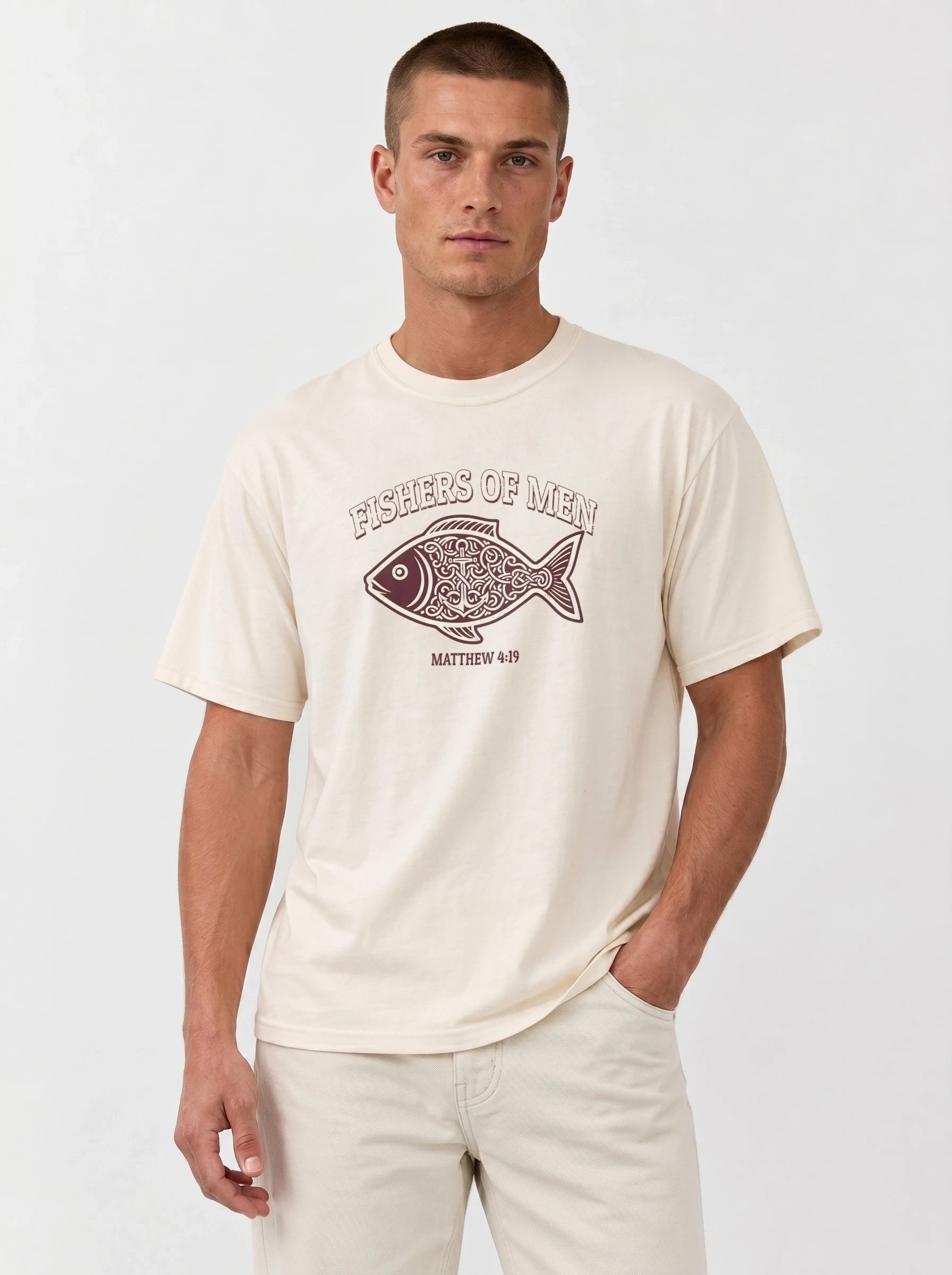 A man wearing a cream-colored crewneck t-shirt with a graphic of a patterned fish and the text 'FISHERS OF MEN' and 'MATTHEW 4:19' on the front, paired with light beige pants, against a plain light gray background.