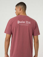 A man wearing a dusty rose short-sleeve t-shirt, viewed from the back. The shirt features the text 'Psalm 23:4' printed in a white Gothic font, with smaller white text underneath, against a plain light gray background.