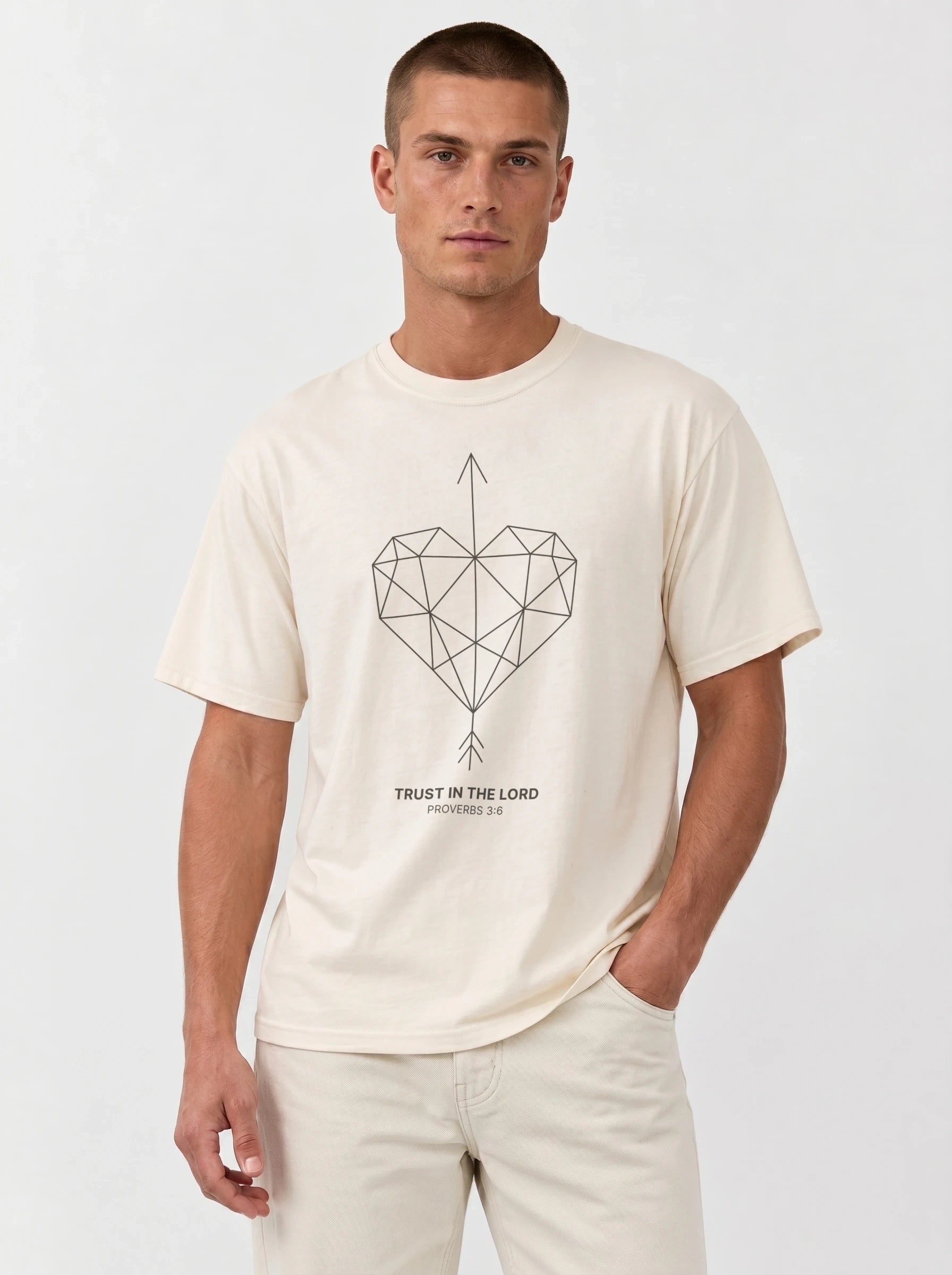 A man wearing a cream-colored short-sleeve t-shirt with a geometric heart pierced by an upward-pointing arrow, paired with the verse Proverbs 3:6: "Trust in the Lord.", paired with matching cream pants, against a plain light gray background.