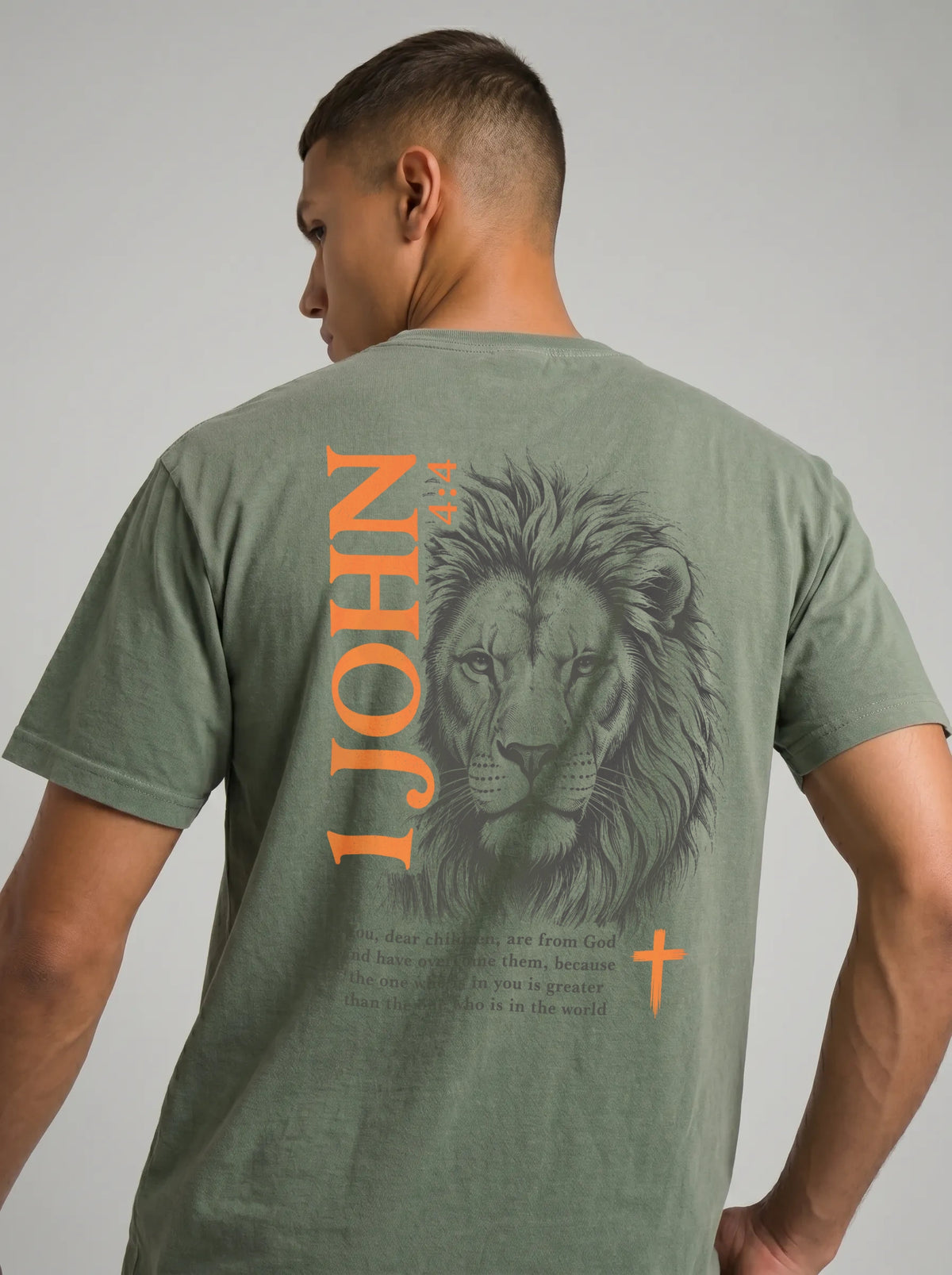 Person wearing a green T-shirt with a dark lion illustration, orange “1 John 4:4” and cross, and the verse “You, dear children, are from God and have overcome them, because the one who is in you is greater than the one who is in the world.”