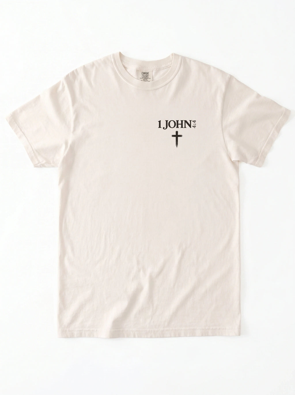 Cream T-shirt laid flat with black “1 John 4:4” text and a cross printed on the chest.