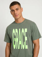 Close-up of a person wearing a muted green T-shirt with large neon green text reading “GRACE.”