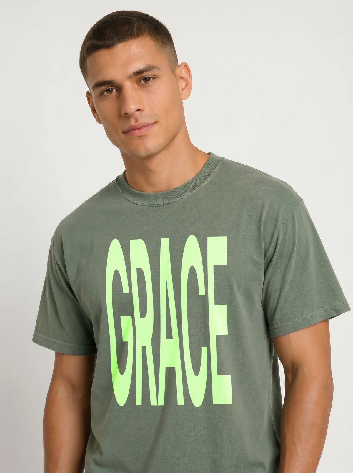 Close-up of a person wearing a muted green T-shirt with large neon green text reading “GRACE.”