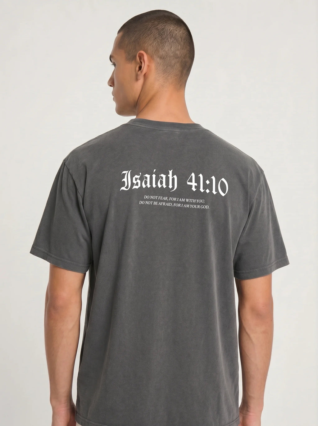 A man viewed from the back wearing a dark gray washed t-shirt with 'Isaiah 41:10' printed in white gothic lettering across the upper back.
