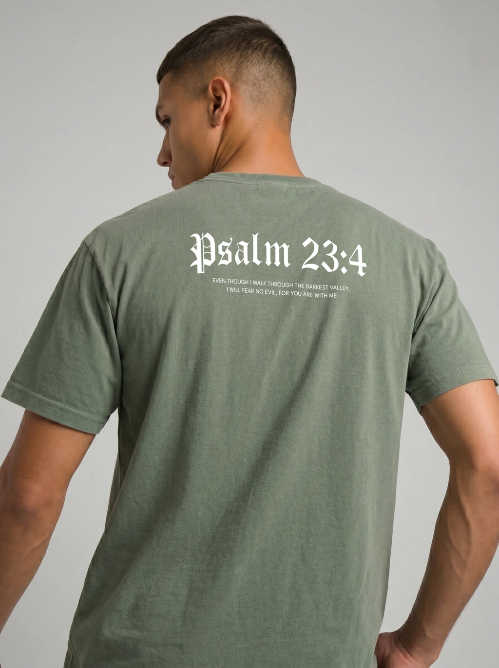 A man wearing an olive green t-shirt, viewed from the back. The shirt features the text 'Psalm 23:4' printed in a white gothic font, with a smaller bible verse underneath, set against a plain light gray background.
