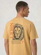 Person wearing a yellow T-shirt with a dark lion illustration, orange “1 John 4:4” and cross, and the verse “You, dear children, are from God and have overcome them, because the one who is in you is greater than the one who is in the world.”