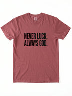 Faded red T-shirt laid flat with black text reading “Never luck. Always God.”