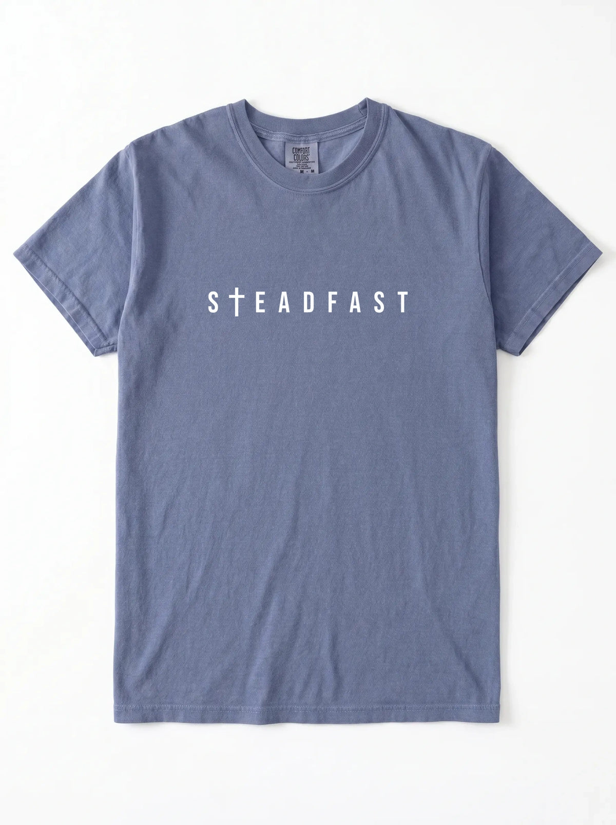 Faded blue short-sleeve T-shirt laid flat with white “Steadfast” text, featuring a cross in place of the letter T.