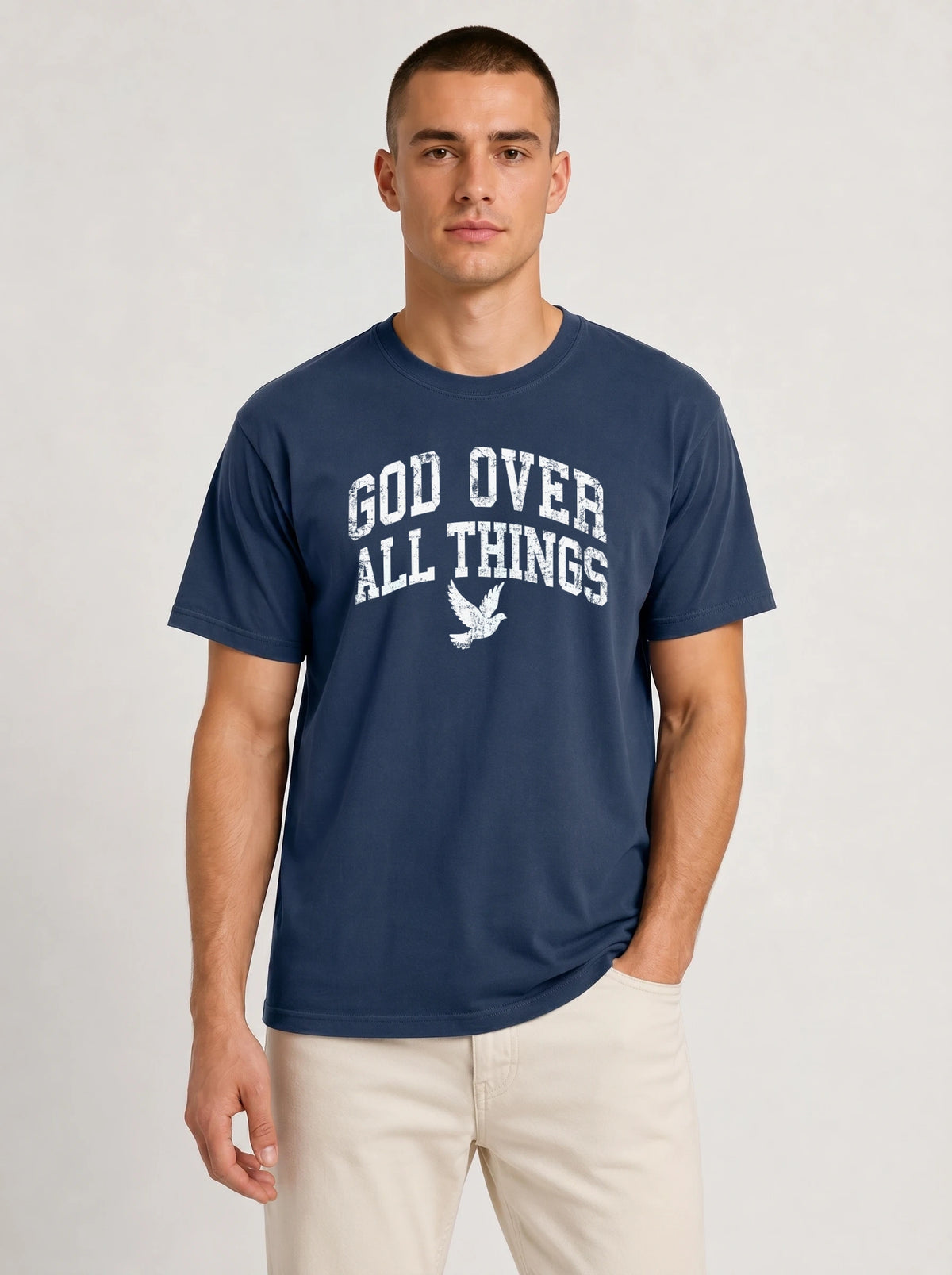 Medium front shot of a male model wearing a dark navy blue short-sleeve t-shirt and light beige shorts, featuring the "GOD OVER ALL THINGS" distressed white text and dove design.