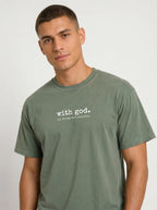 A man wearing a muted sage green t-shirt with the white printed text 'with god. all things are possible' on the chest, photographed against a light gray studio background.