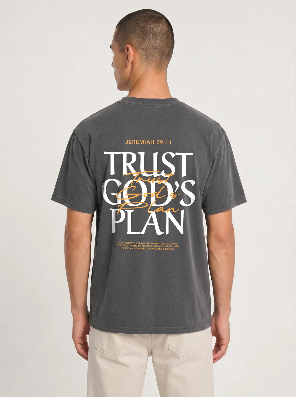 Person wearing a faded charcoal T-shirt with a large back design reading “JEREMIAH 29:11” and “TRUST GOD’S PLAN,” with the verse below.