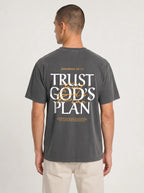 Person wearing a faded charcoal T-shirt with a large back design reading “JEREMIAH 29:11” and “TRUST GOD’S PLAN,” with the verse below.