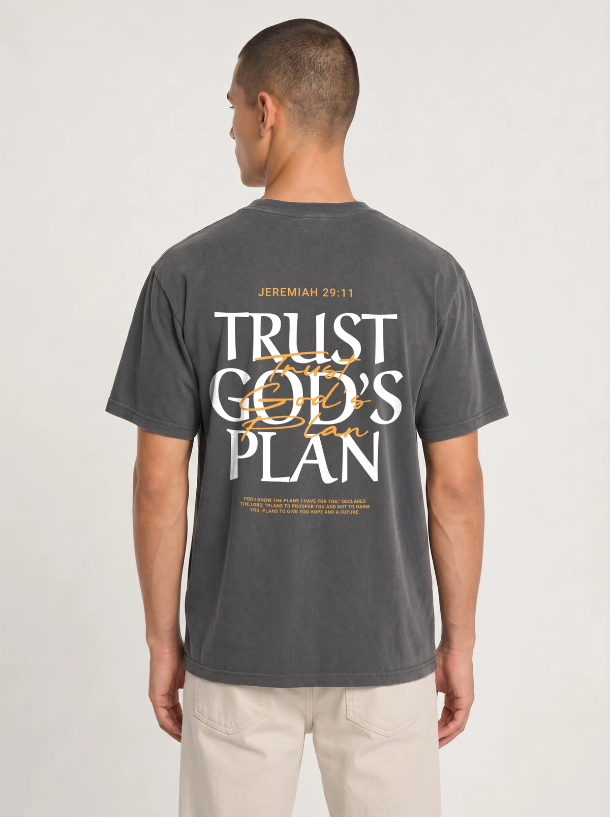 Person wearing a faded charcoal T-shirt with a large back design reading “JEREMIAH 29:11” and “TRUST GOD’S PLAN,” with the verse below.