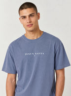Young man modeling a faded blue short-sleeve T-shirt featuring white “JESUS SAVES” text with a small cross below, posed against a plain light background.