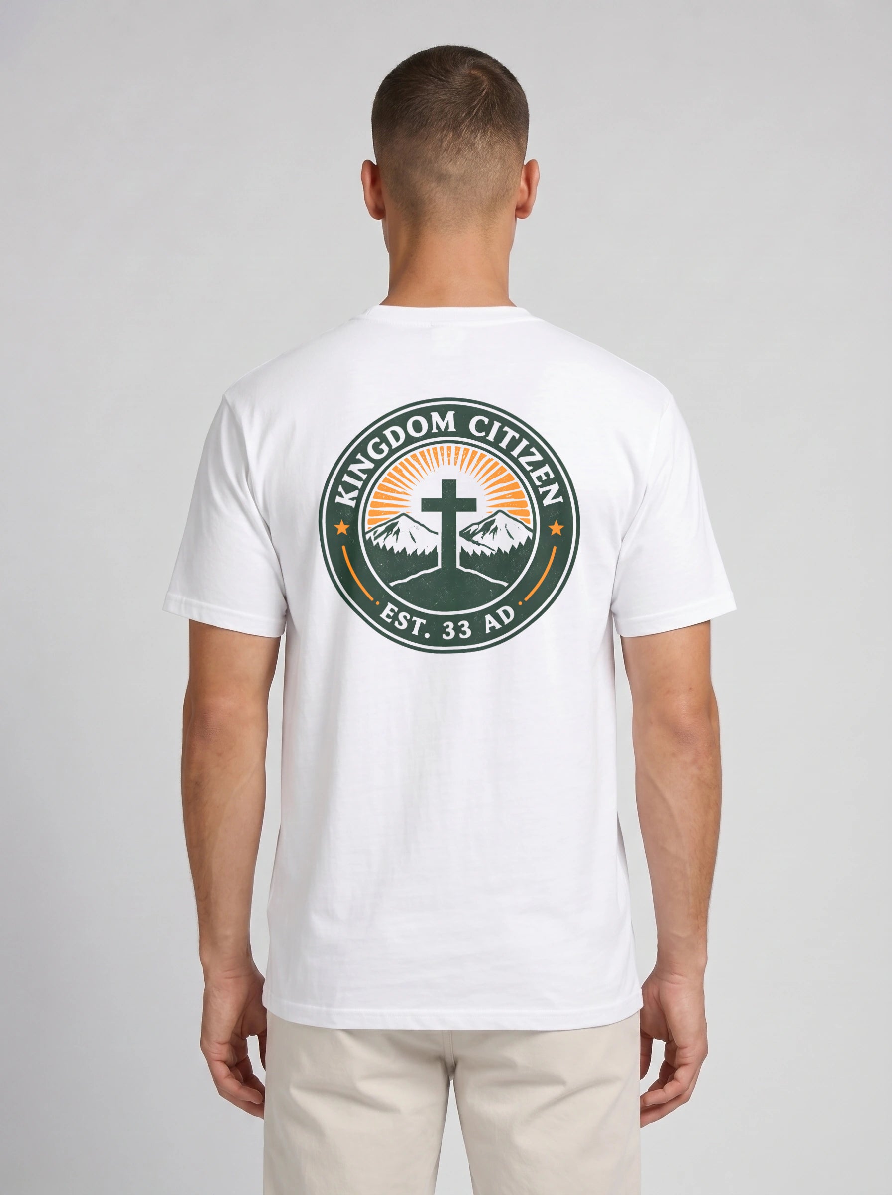A man viewed from the back wearing a white short-sleeve t-shirt with a large circular graphic on the back. The graphic features a green border with the text 'KINGDOM CITIZEN' and 'EST. 33 AD.