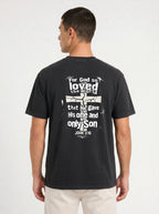 A man wearing a dark charcoal gray t-shirt, viewed from the back. The shirt features a distressed white graphic with the text 'For God so loved the world that He gave His one and only Son JOHN 3:16' surrounding a cracked cross design.