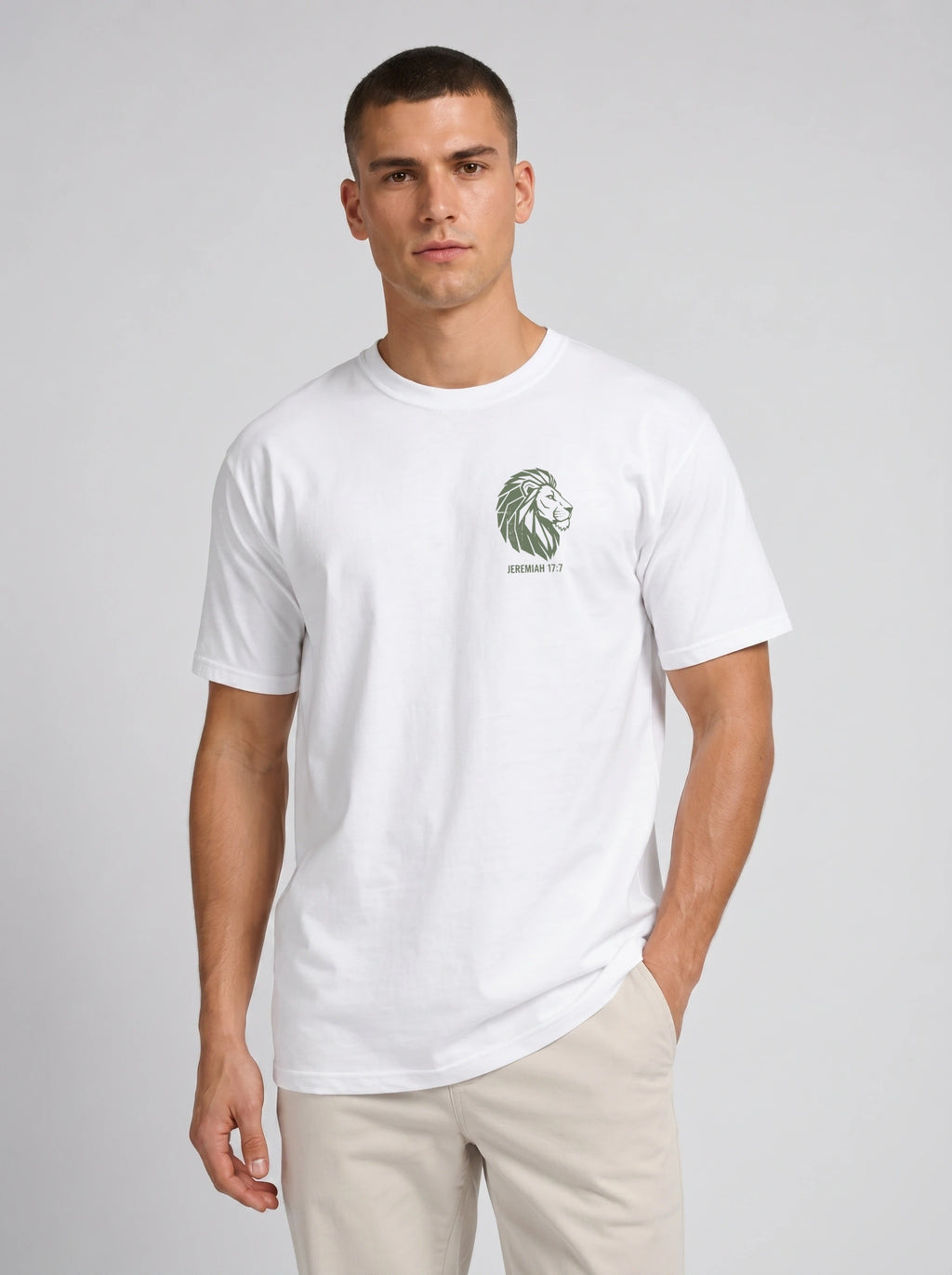 A man wearing a white crew-neck t-shirt with a green lion graphic and 'JEREMIAH 17:7' text on the left chest, paired with beige trousers, against a light gray studio background.