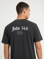 A man wearing a faded black t-shirt, viewed from the back. The shirt features the text 'John 14:6 THE WAY THE TRUTH THE LIFE' printed in a white gothic font on the upper back.
