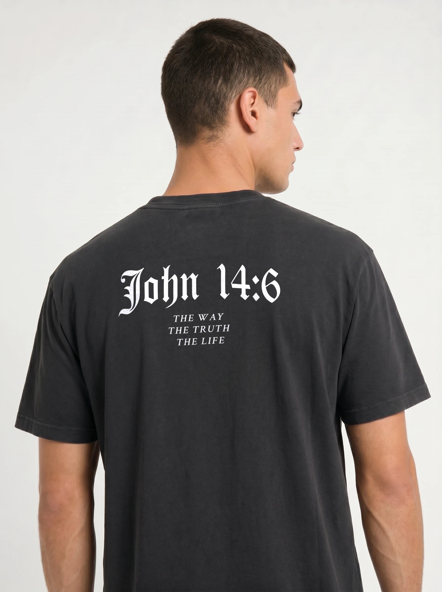 A man wearing a faded black t-shirt, viewed from the back. The shirt features the text 'John 14:6 THE WAY THE TRUTH THE LIFE' printed in a white gothic font on the upper back.