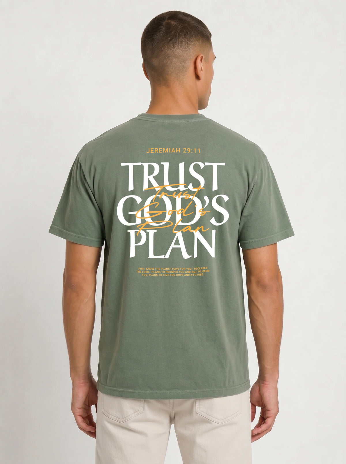 Person wearing a muted green T-shirt with a large back design reading “JEREMIAH 29:11” and “TRUST GOD’S PLAN,” with the verse below.