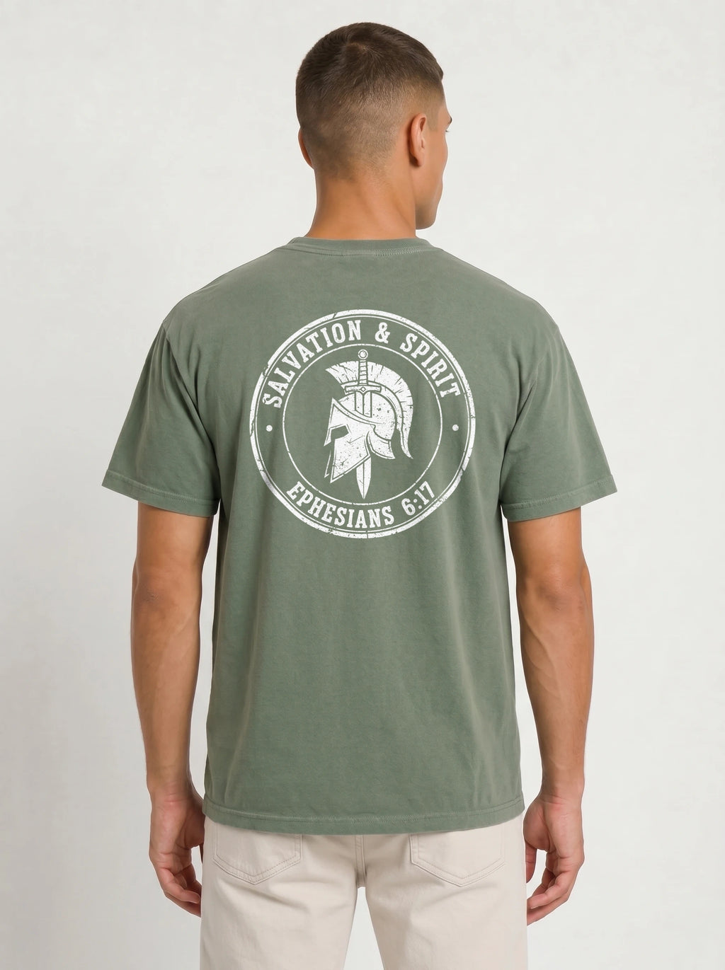 A man viewed from the back wearing an olive green t-shirt with a large white graphic print on the back featuring a Spartan helmet and the text 'SALVATION & SPIRIT' and 'EPHESIANS 6:17'.