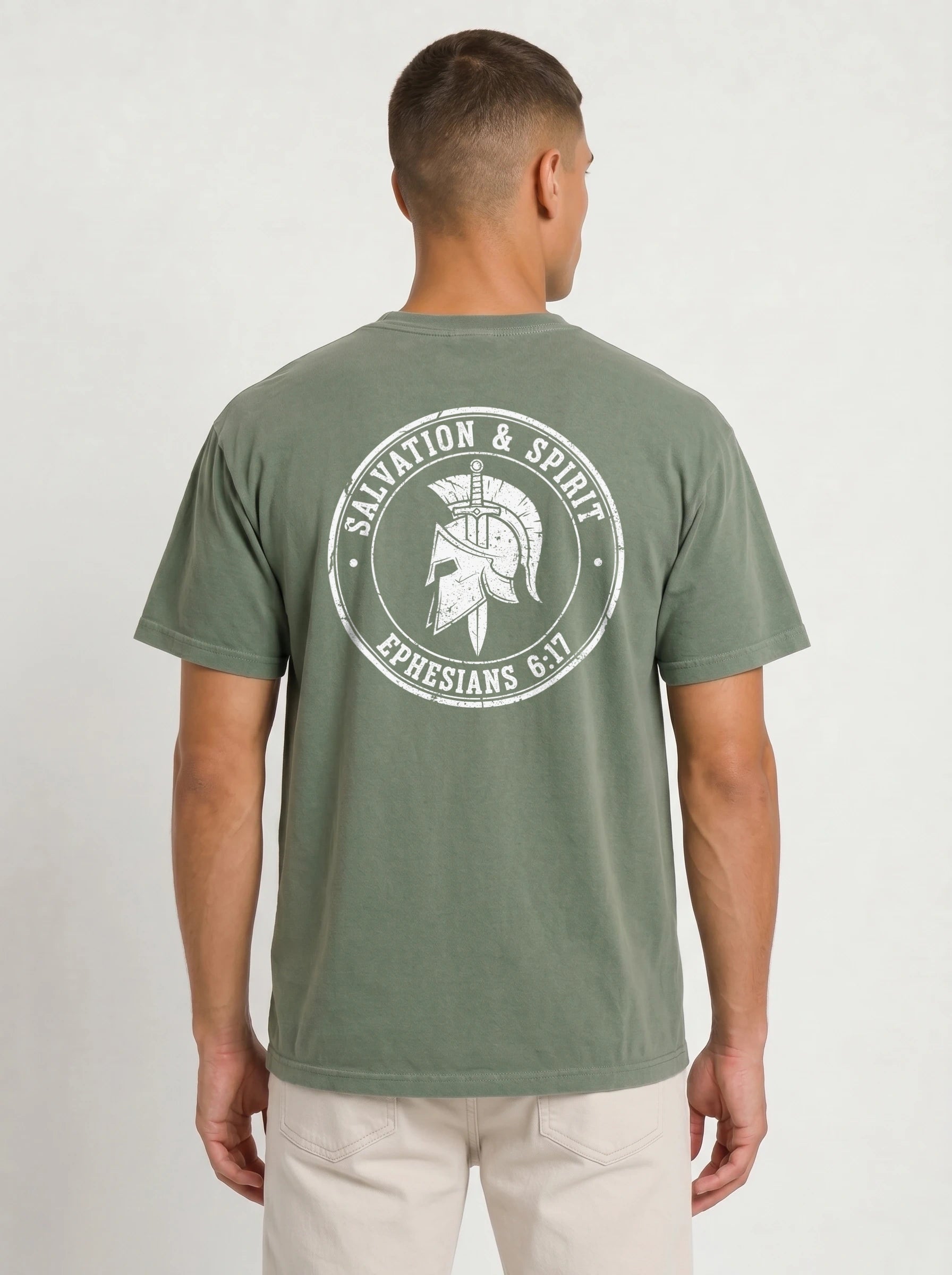 A man viewed from the back wearing an olive green t-shirt with a large white graphic print on the back featuring a Spartan helmet and the text 'SALVATION & SPIRIT' and 'EPHESIANS 6:17'.