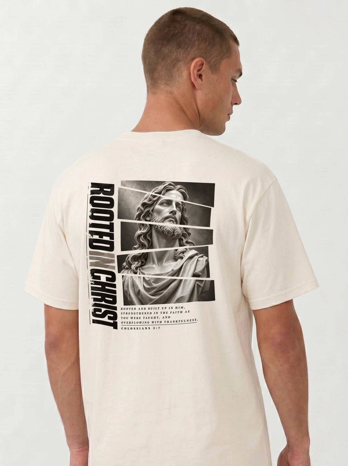 Person turned sideways wearing a cream T-shirt with a grayscale Jesus graphic, vertical “Rooted in Christ” text, and Colossians 2:7.