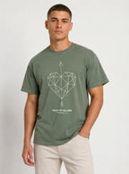 A man wearing an olive green crewneck t-shirt with a geometric heart pierced by an upward-pointing arrow, paired with the verse Proverbs 3:6: "Trust in the Lord.", paired with light beige pants, against a plain light gray background.