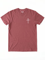 A dusty rose short-sleeve crewneck t-shirt with a small white cross graphic on the left chest, displayed flat against a white background.