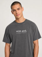 A man wearing a dark gray mineral-wash t-shirt with a vertical white line graphic and the text 'with god. all things are possible' printed on the chest, set against a plain light gray background.