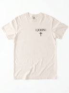 Cream T-shirt laid flat with “1 John 4:4” and a cross printed on the chest.
