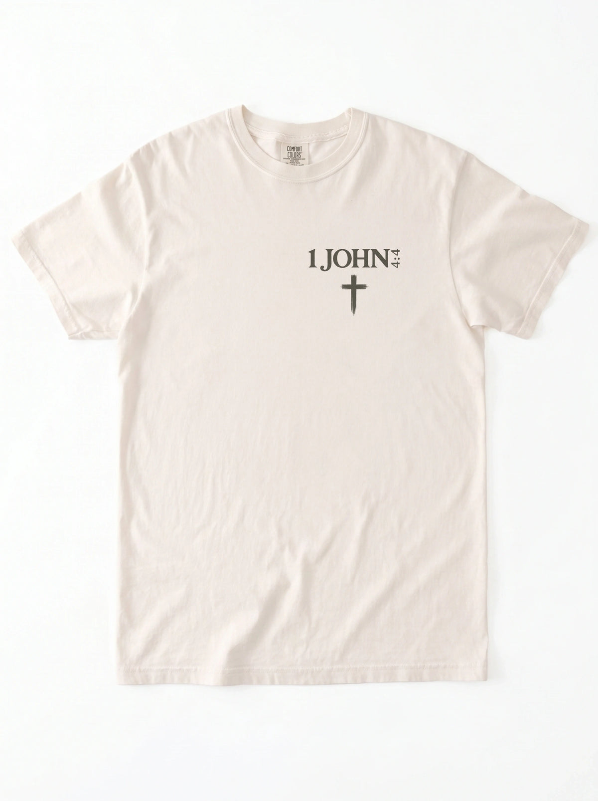 Cream T-shirt laid flat with “1 John 4:4” and a cross printed on the chest.