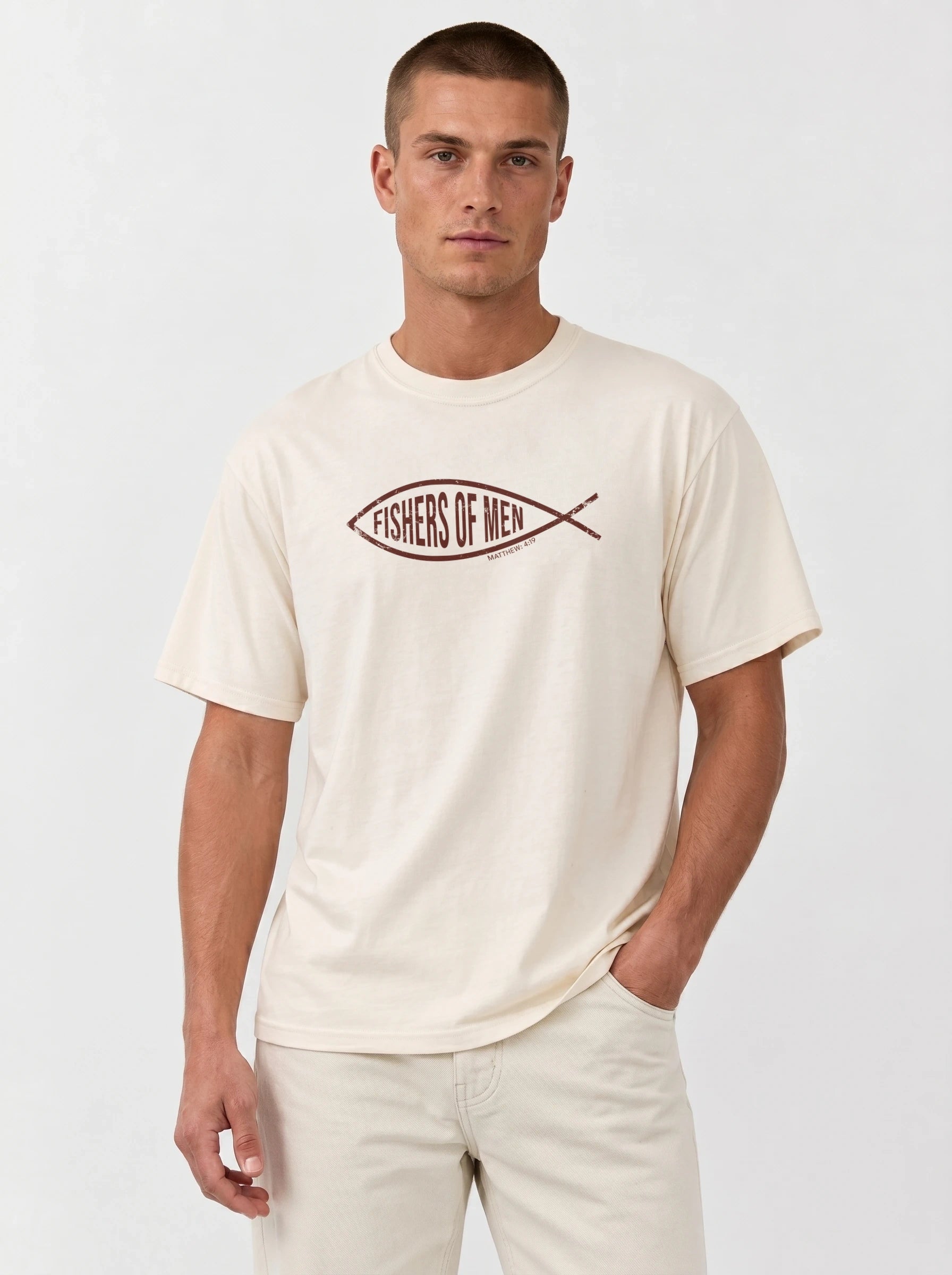 A man wearing a cream-colored t-shirt with a brown fish graphic that reads 'FISHERS OF MEN' across the chest, paired with matching cream pants, against a plain light gray background.