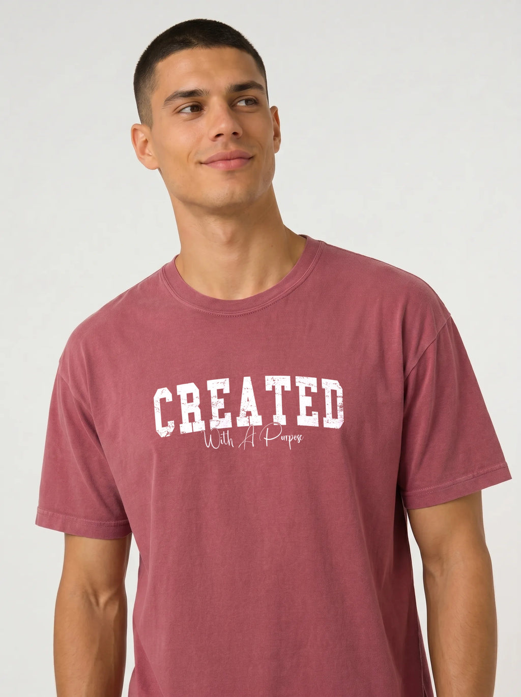 A man wearing a heathered dusty rose t-shirt with 'CREATED With A Purpose' printed in white on the chest, photographed against a light gray studio background.
