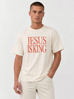 Person wearing a cream T-shirt with distressed orange text reading “Jesus Is King.”