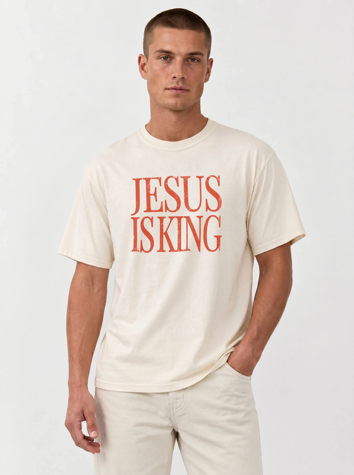Person wearing a cream T-shirt with distressed orange text reading “Jesus Is King.”