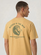 A man shown from the back wearing a mustard yellow t-shirt with a green graphic print featuring a lion head and the text 'BLESSED IS THE MAN WHOSE CONFIDENCE IS IN HIM'.