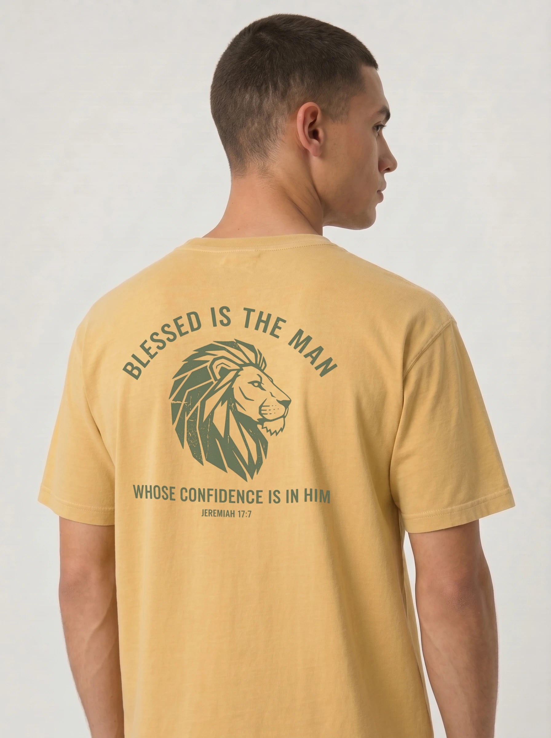 A man shown from the back wearing a mustard yellow t-shirt with a green graphic print featuring a lion head and the text 'BLESSED IS THE MAN WHOSE CONFIDENCE IS IN HIM'.