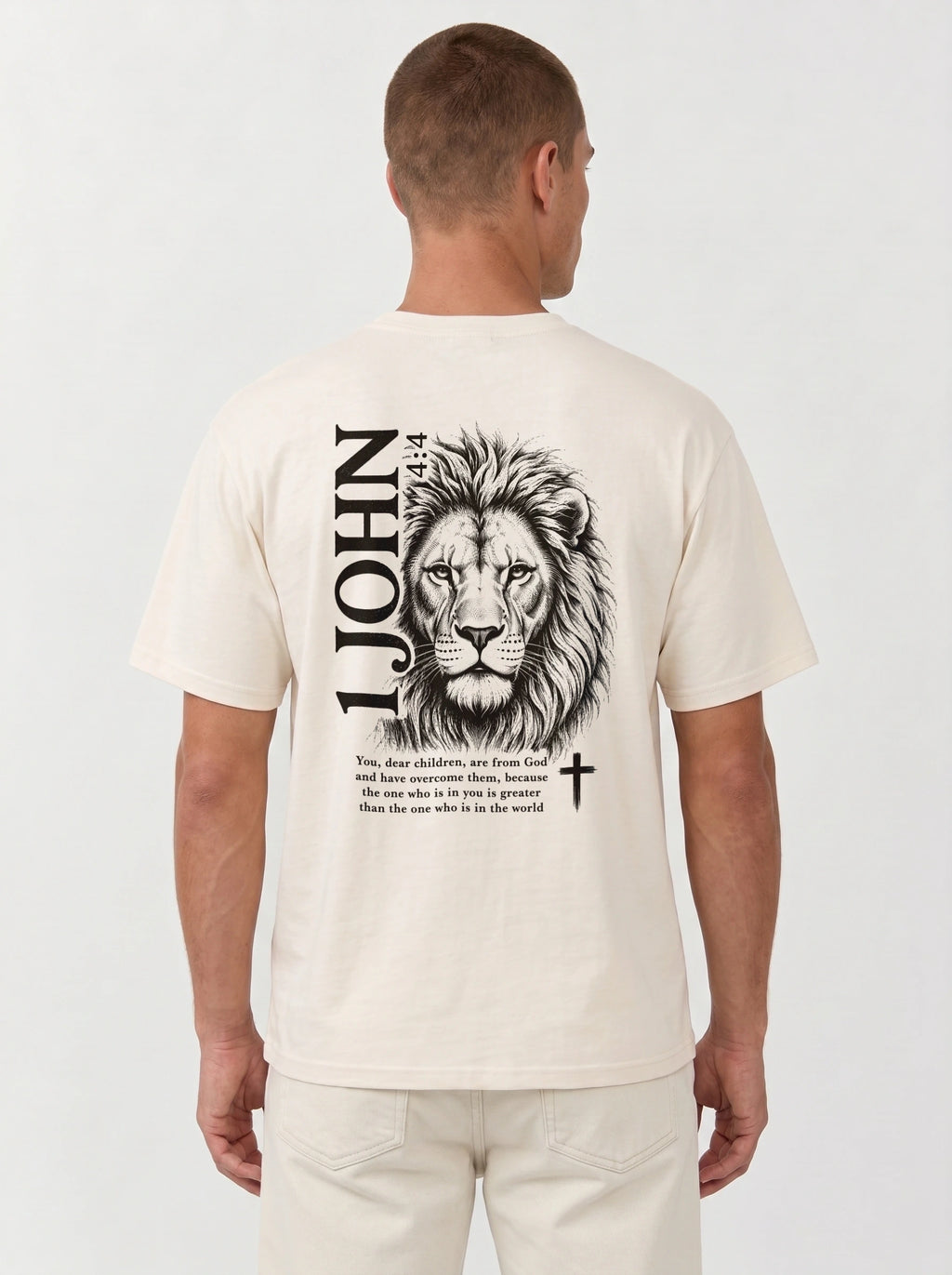 Person wearing a cream T-shirt with a black lion illustration, cross, “1 John 4:4,” and the verse text, “You, dear children, are from God and have overcome them, because the one who is in you is greater than the one who is in the world.”