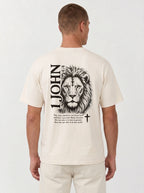 Person wearing a cream T-shirt with a black lion illustration, cross, “1 John 4:4,” and the verse text, “You, dear children, are from God and have overcome them, because the one who is in you is greater than the one who is in the world.”