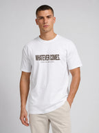 A man wearing a white crew-neck t-shirt with the text 'WHATEVER COMES. GOD REMAINS.