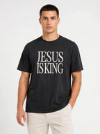 Person wearing a black T-shirt with distressed cream text reading “Jesus Is King.”