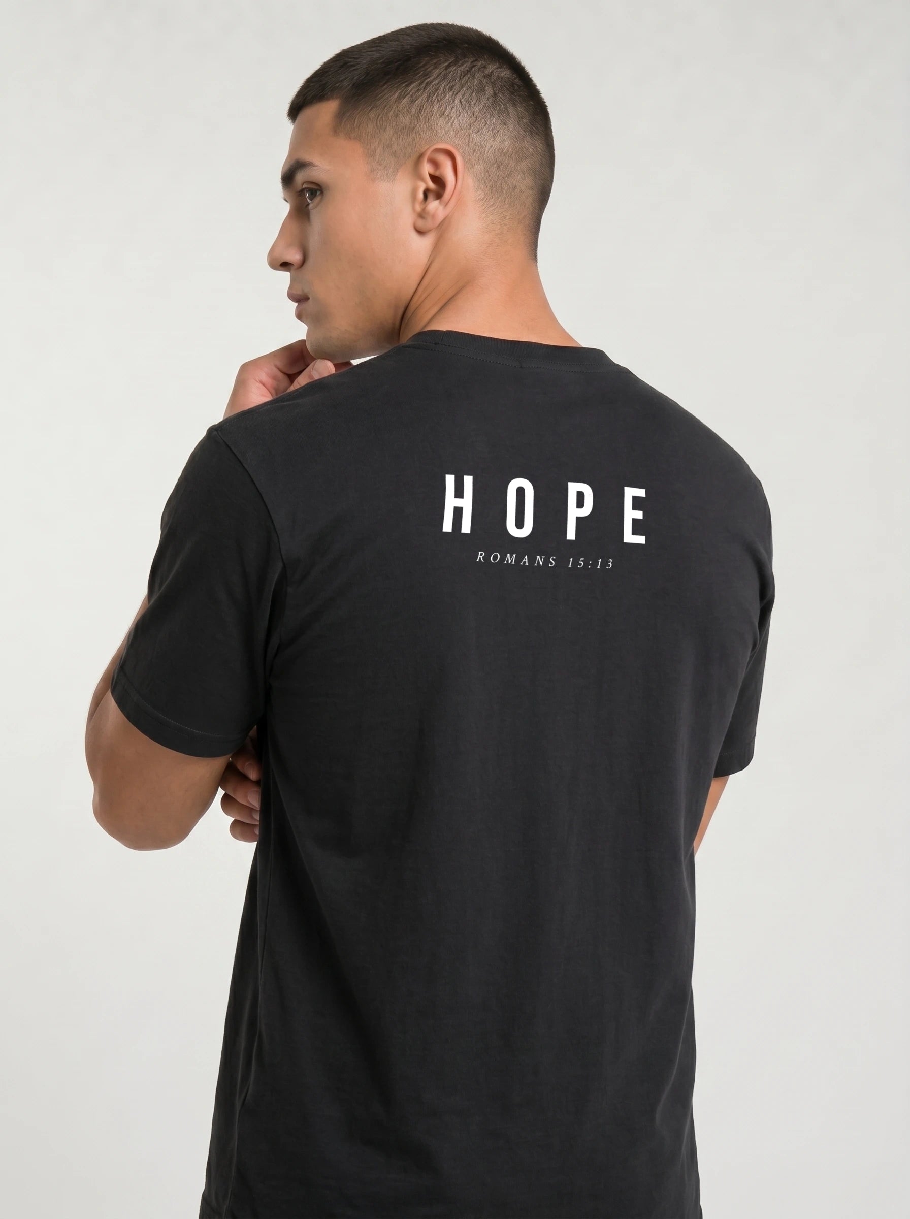 A man wearing a black t-shirt, viewed from the back. The shirt features the word 'HOPE' printed in white block letters with 'ROMANS 15:13' underneath.