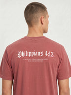 A man viewed from behind wearing a dusty rose short-sleeve t-shirt with white Gothic-style text reading 'Philippians 4:13' and smaller scripture text below, against a light gray background.