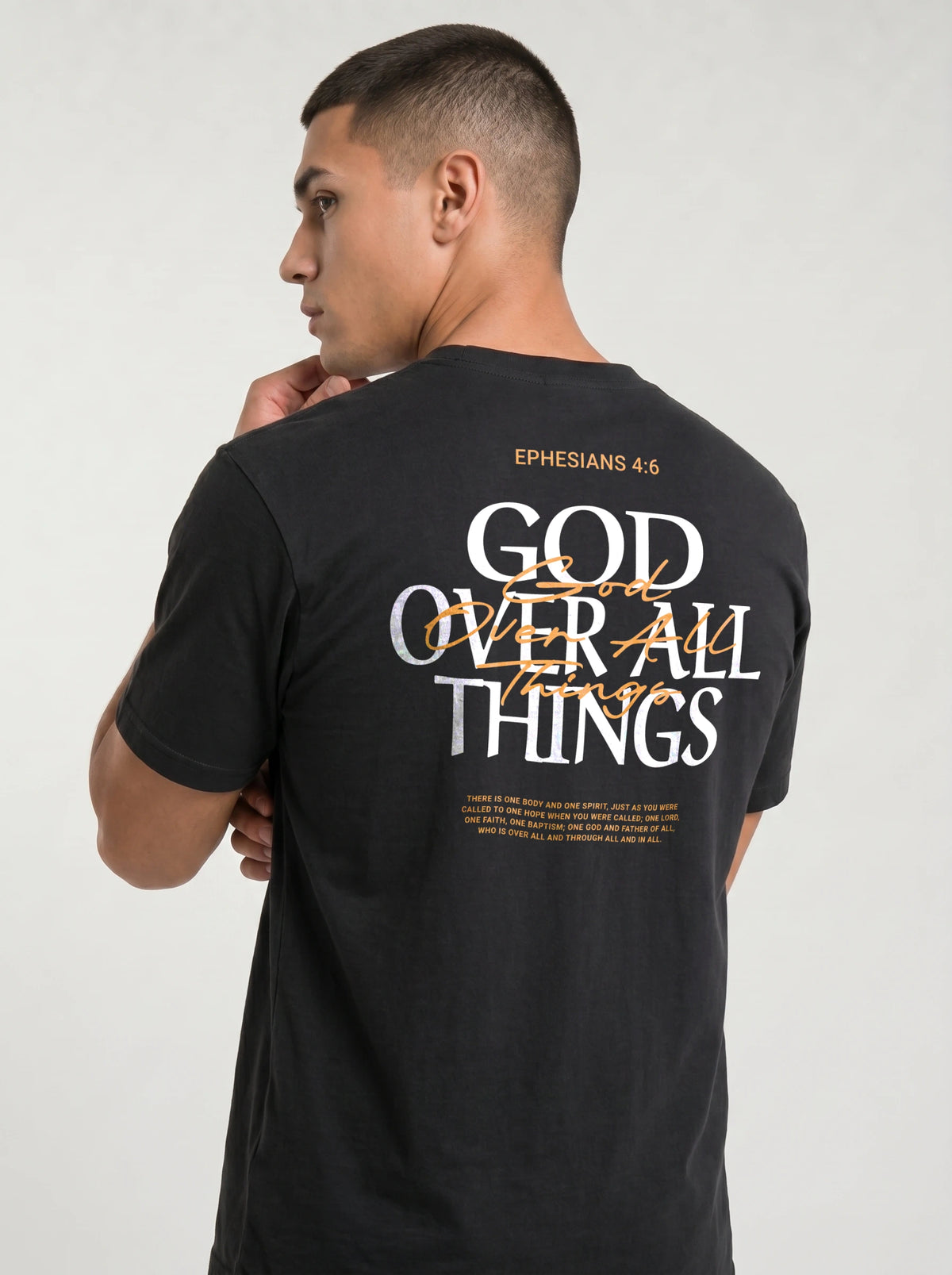 Person wearing a black T-shirt with “Ephesians 4:6,” a large white and orange “God Over All Things” back graphic, and Bible verse text.