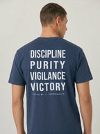 Person wearing a navy T-shirt with large back text reading “Discipline Purity Vigilance Victory” and “Overcome // 1 Corinthians 9:25.”
