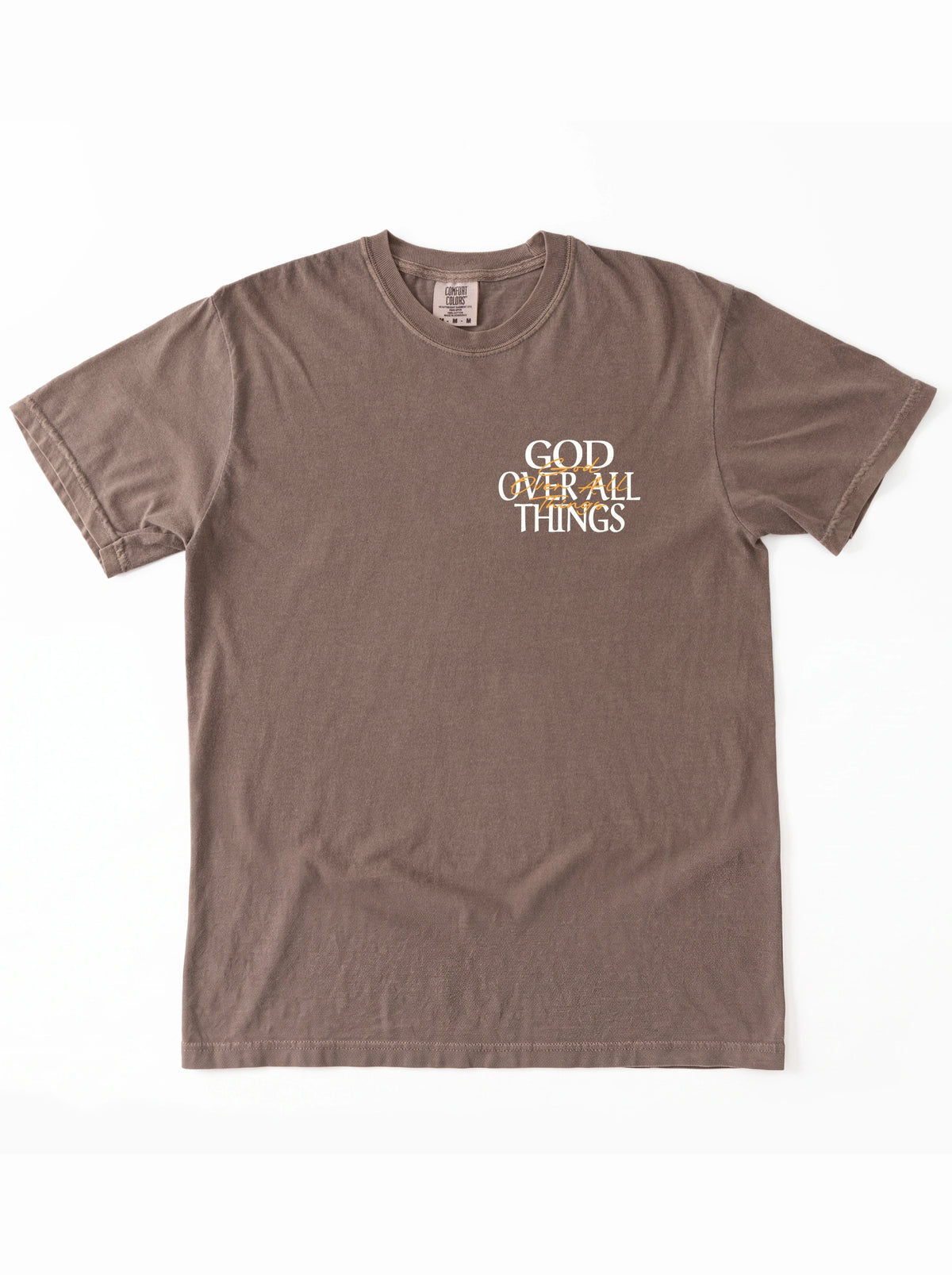 Brown T-shirt laid flat with a small white and orange chest graphic reading “God Over All Things.”