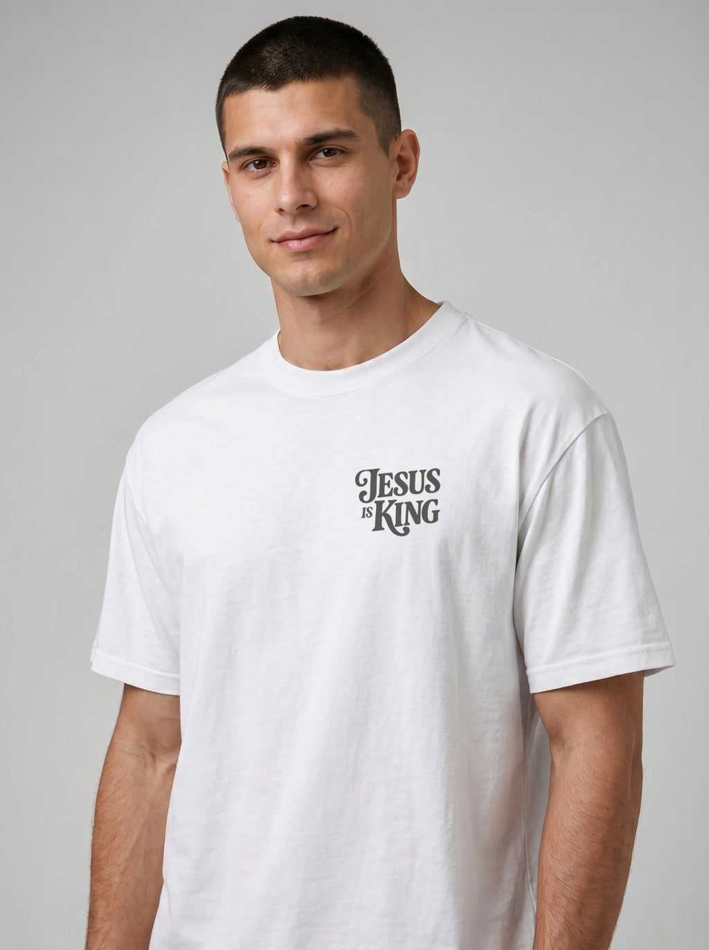 Person wearing a white T-shirt with a small dark “Jesus is King” design on the left chest.