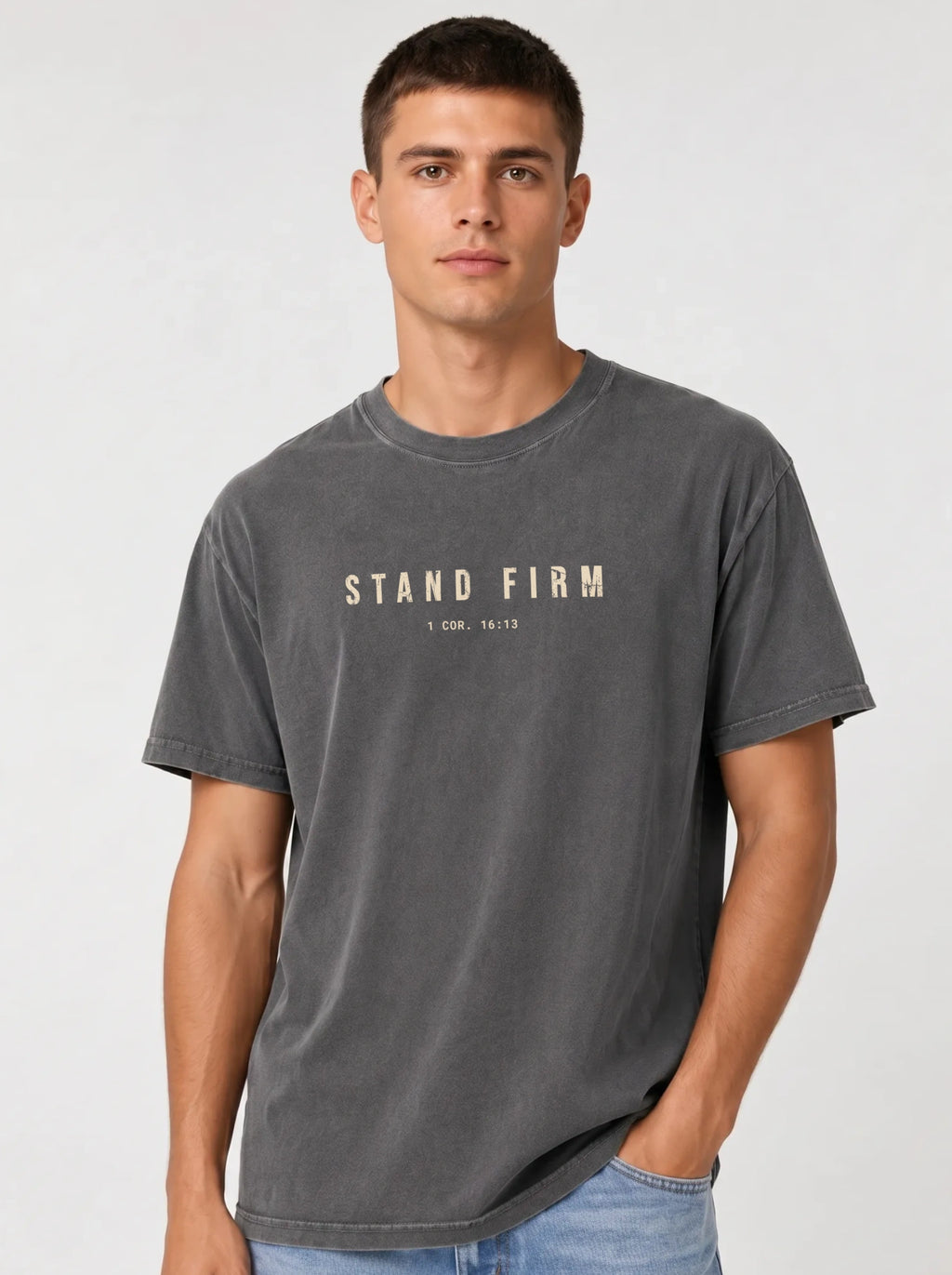 Person wearing a faded gray T-shirt with distressed beige text reading “Stand Firm” and “1 Cor. 16:13.”
